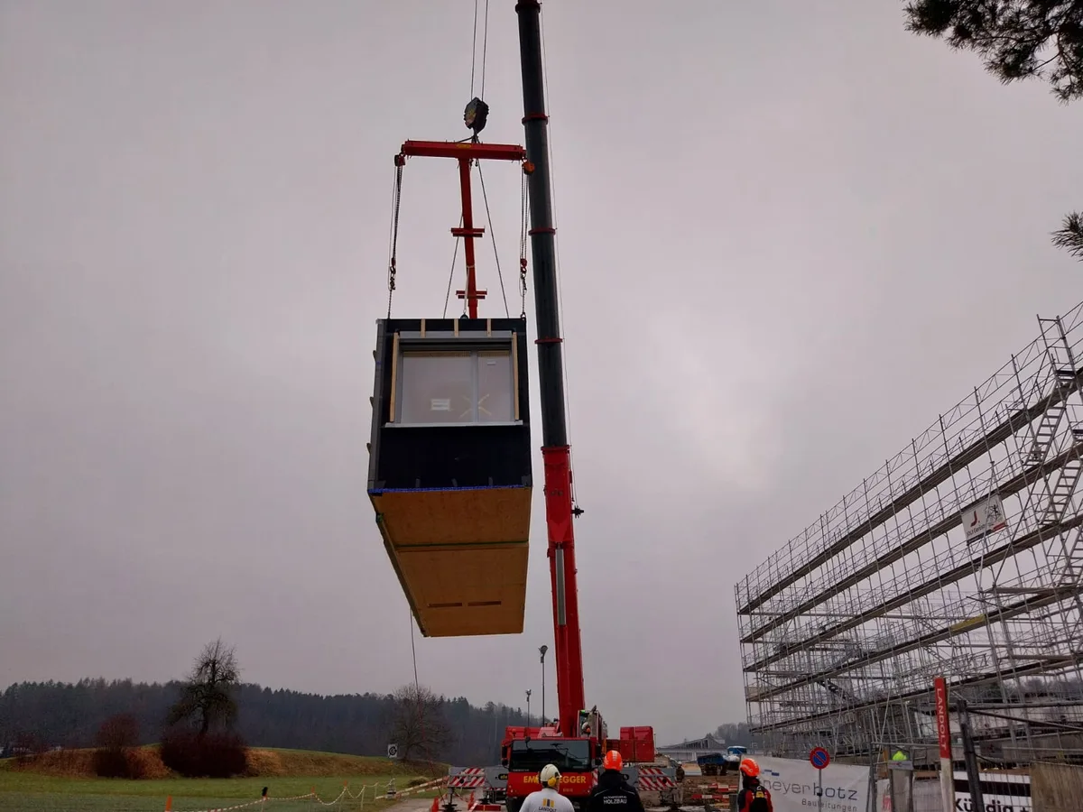Ein Kran hievt ein Holzmodul auf die Baustelle.